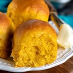 three pumpkin dinner rolls on a white plate with butter on the side
