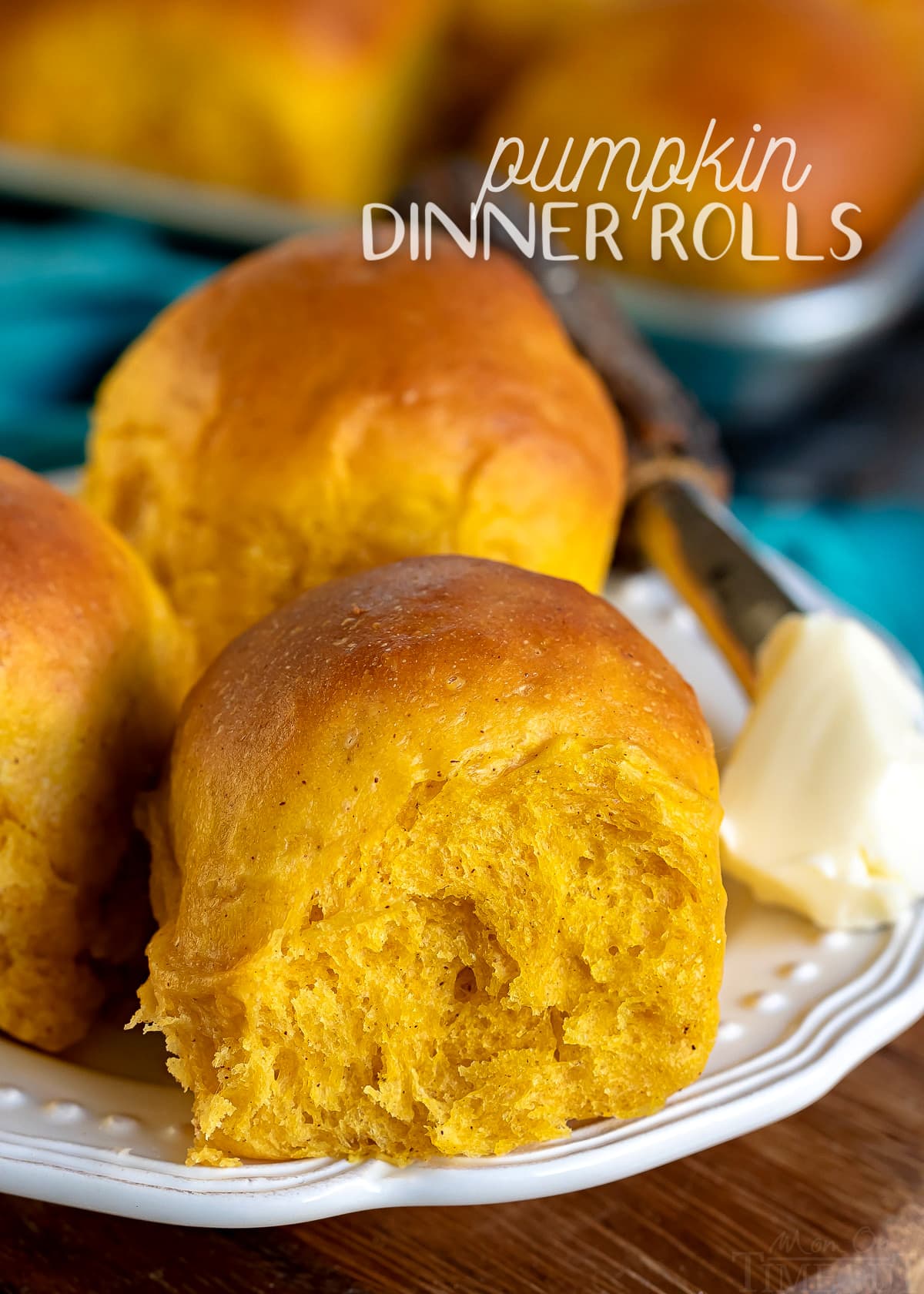 three pumpkin dinner rolls on a white plate with butter on the side