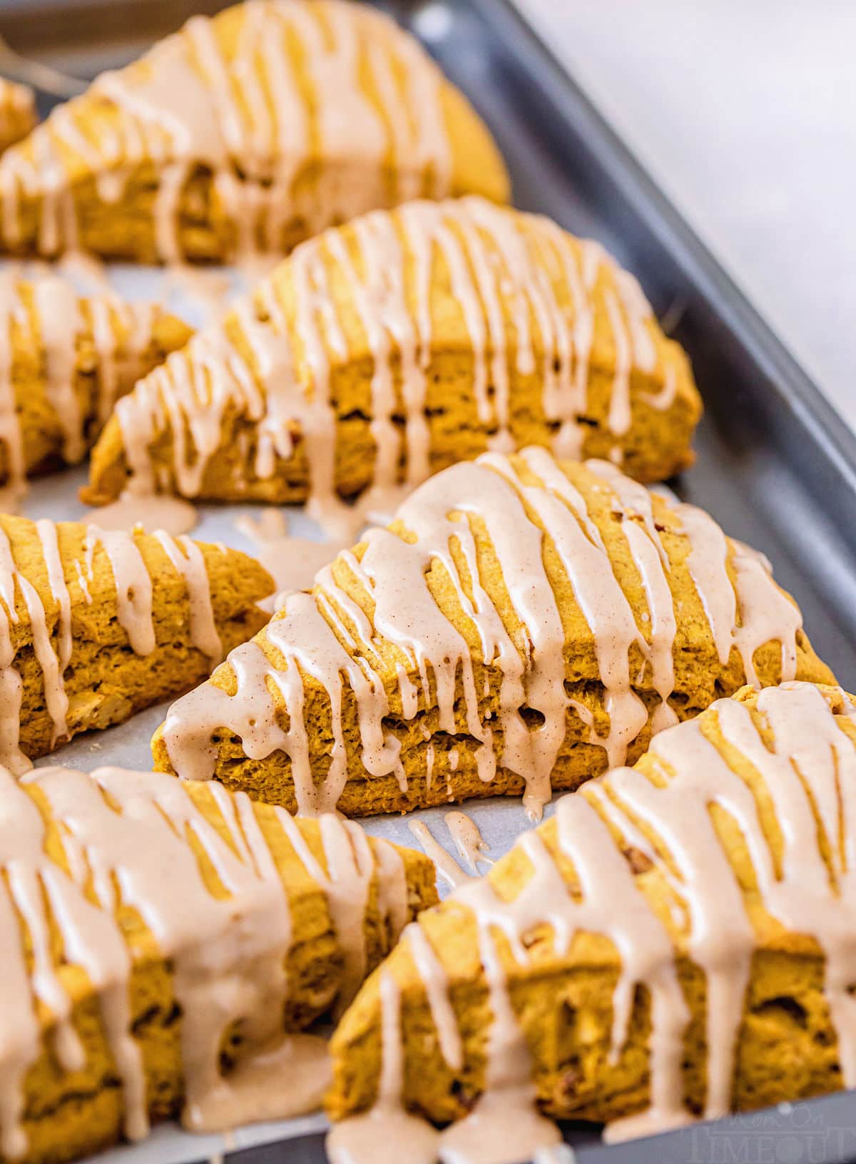 pumpkin scones on baking sheet with glaze drizzled on