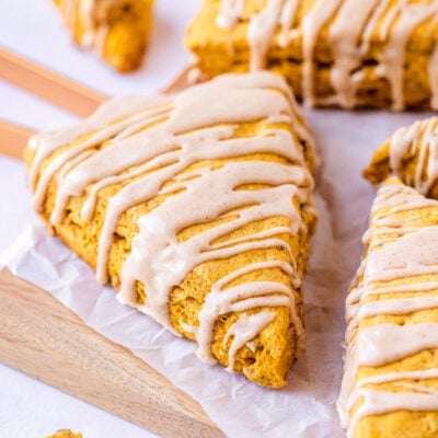 pumpkin scones sitting on white parchment on a wood cutting board with a maple cinnamon glaze