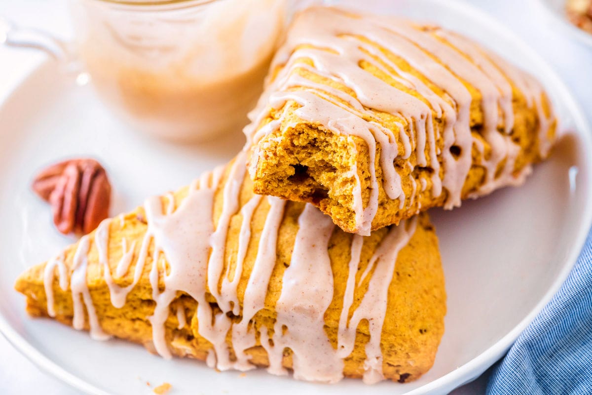 pumpkin scones with bite taken on white plate next to a blue napkin