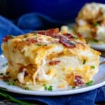 serving of scalloped potatoes made with bacon and onion on a small white plate with a blue napkin underneath it.