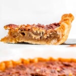 slice of pecan pie on pie server with pie beneath