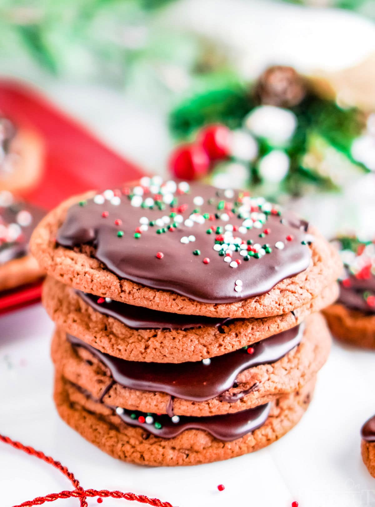 stack of 4 chocolate cookies all glazes with sprinkles and christmas decor in the background