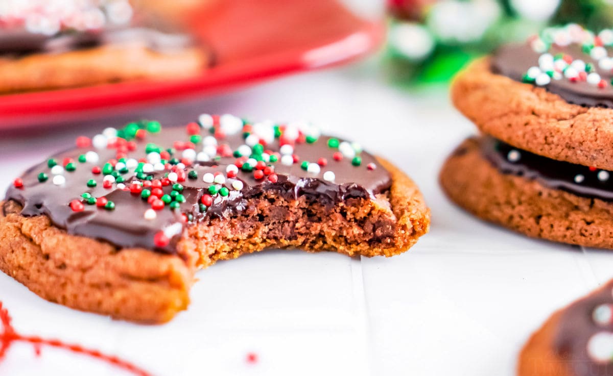 cookie with bite out of it sitting on white surface with more chocolate cookies in background