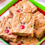 reindeer cookie bars decorated with pretzels m&ms and mini chocolate chips sitting in Christmas box