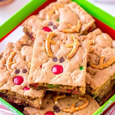 reindeer cookie bars decorated with pretzels m&ms and mini chocolate chips sitting in Christmas box