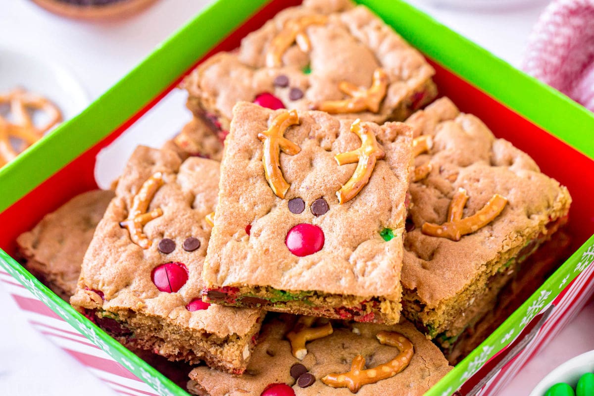 reindeer cookie bars decorated with pretzels m&ms and mini chocolate chips sitting in Christmas box
