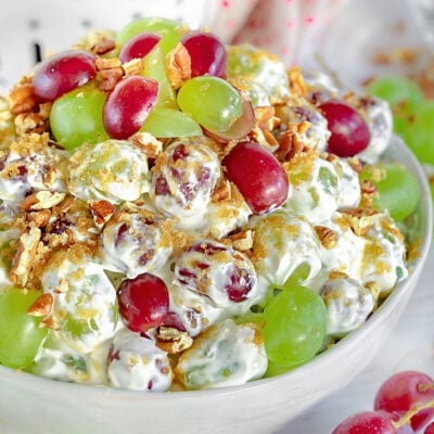 front view of creamy grape salad in white bowl with grapes scattered around