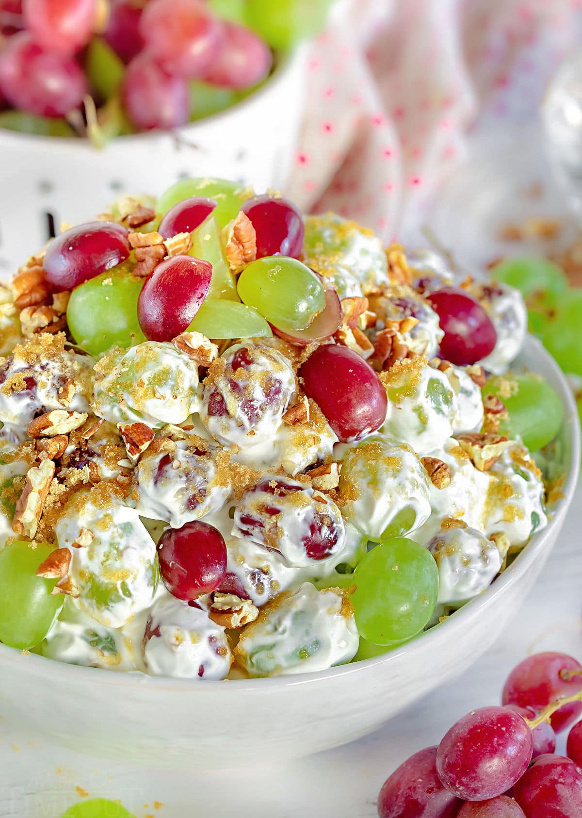 front view of creamy grape salad in white bowl with grapes scattered around