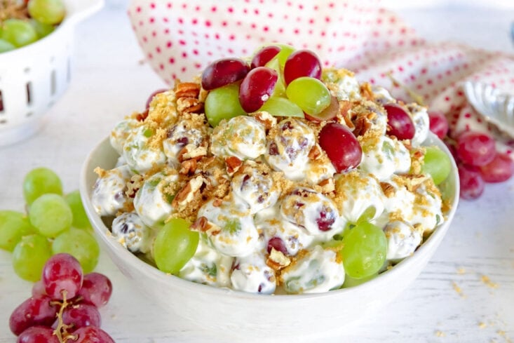 grape salad with creamy cream cheese dressing topping with brown sugar and pecans in white bowl with grapes around it
