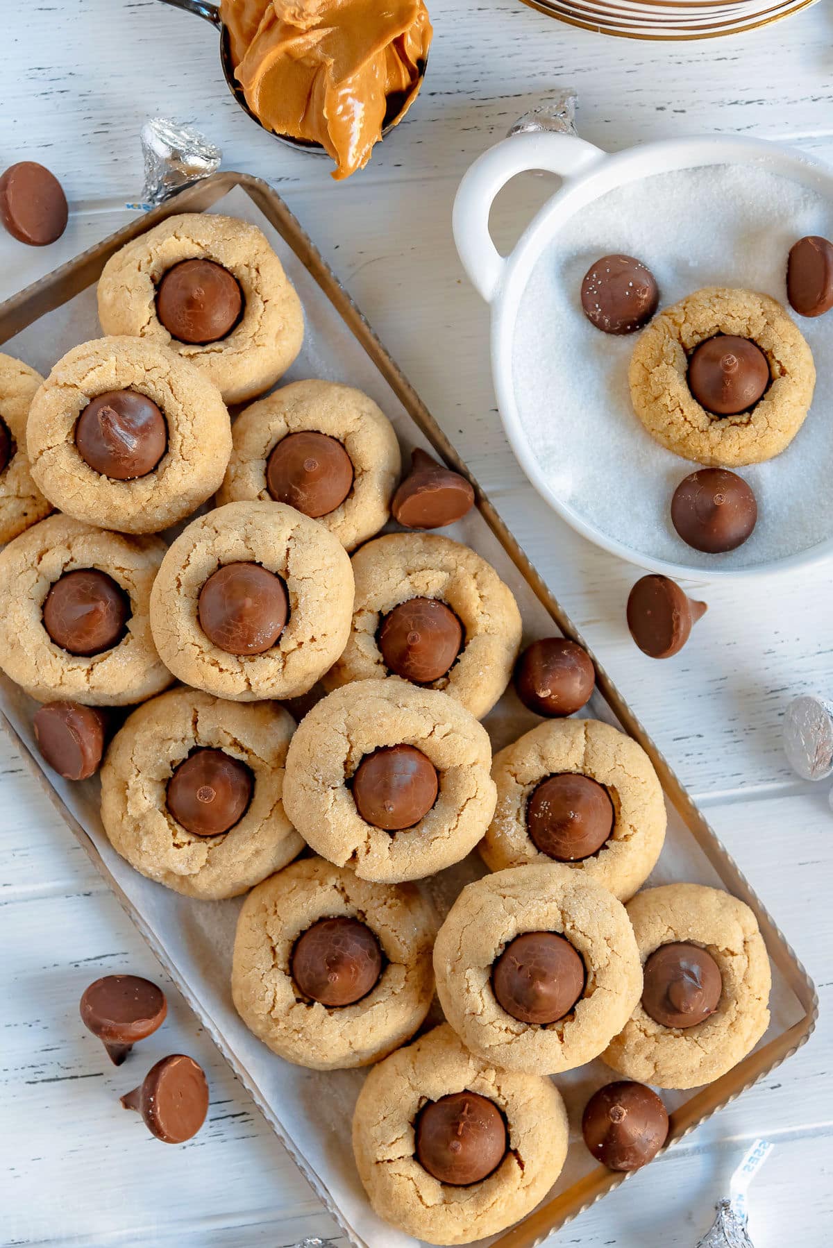 top down of peanut butter blossom cookies on gray metal tray with Hershey's kisses scattered about