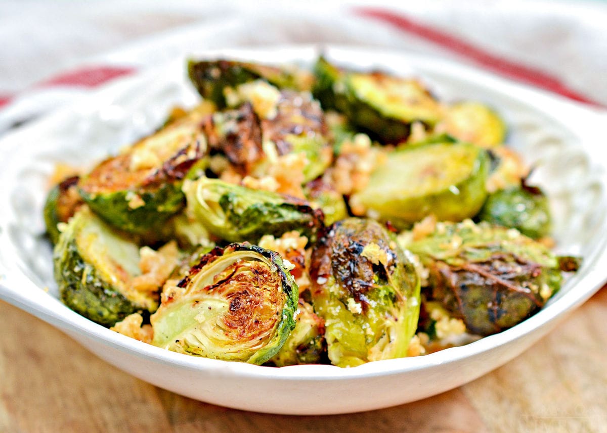 brussels sprouts in white shallow bowl made in air fryer with parmesan and garlic and white and red towel in background