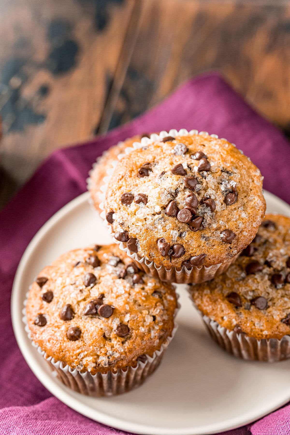 four chocolate chip muffins on a white plate with a burgundy napkin beneath the plate