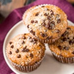 four chocolate chip muffins on a white plate with a burgundy napkin beneath the plate