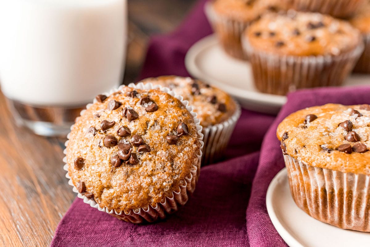 muffins scattered about on plate and burgundy napkin with glass of milk in background