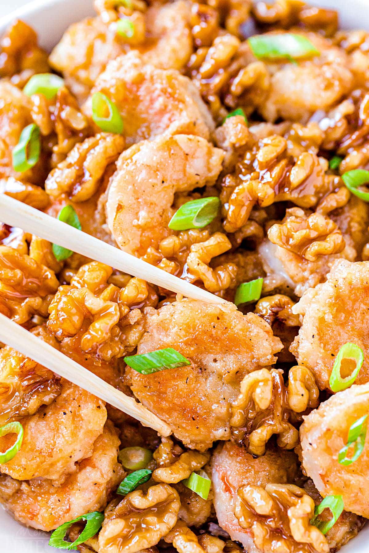 close up look at honey walnut shrimp being held with chopsticks in front of dish