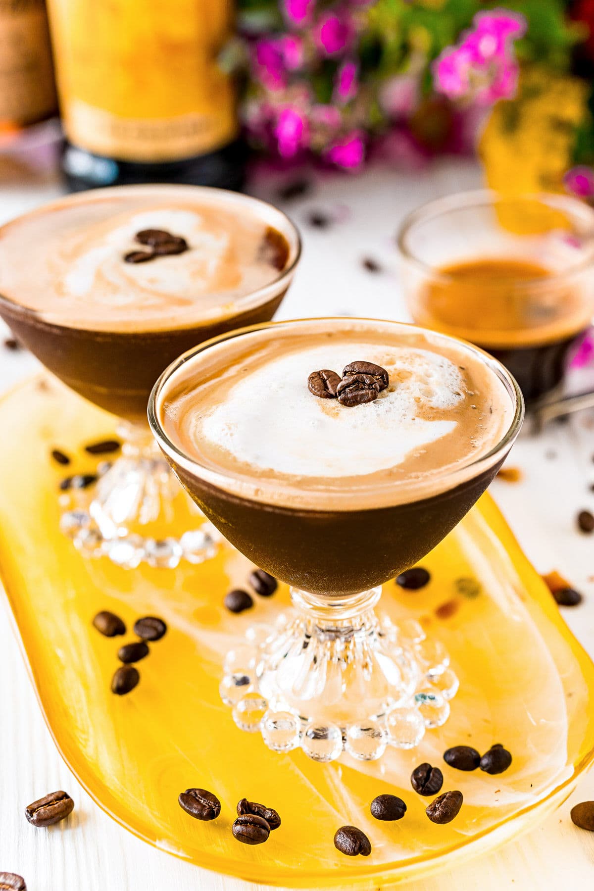 two espresso martinis on a yellow glass tray with espresso beans scattered about