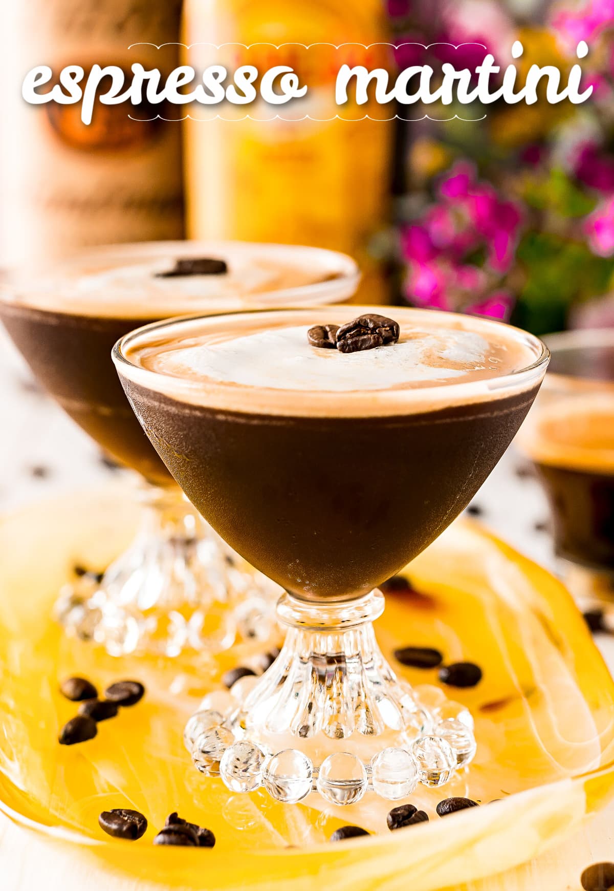 two espresso martini in fancy martini glass on yellow tray with title overlay at top of image and bottles in background