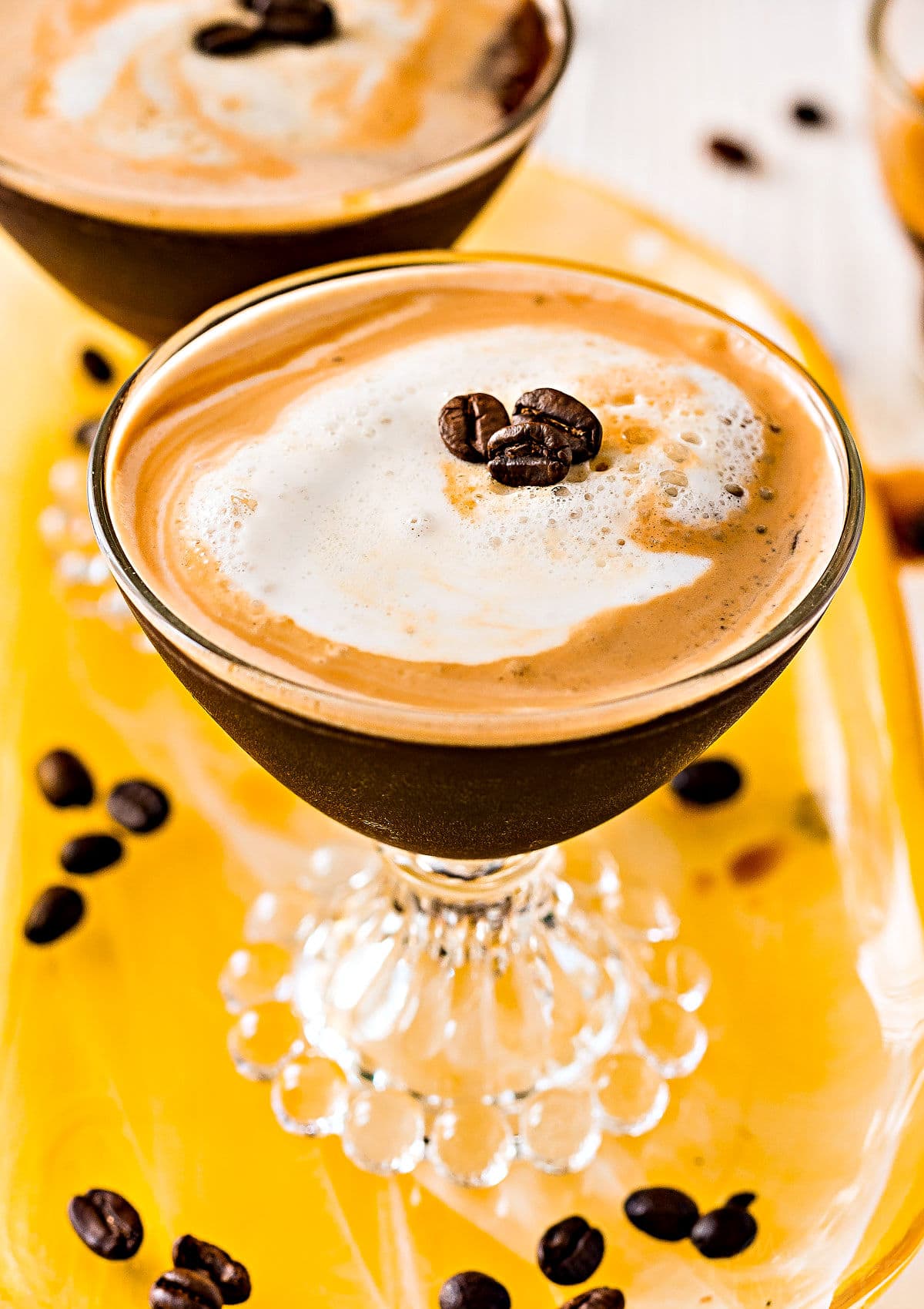 espresso martini recipe in two glasses on yellow glass tray top down view