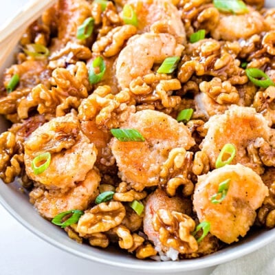 close look at honey walnut shrimp in white bowl garnished with green onion
