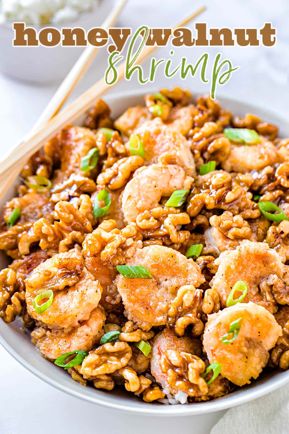 honey walnut shrimp in a white bowl garnished with green onions with chopsticks on edge of bowl and title overlay at top of image
