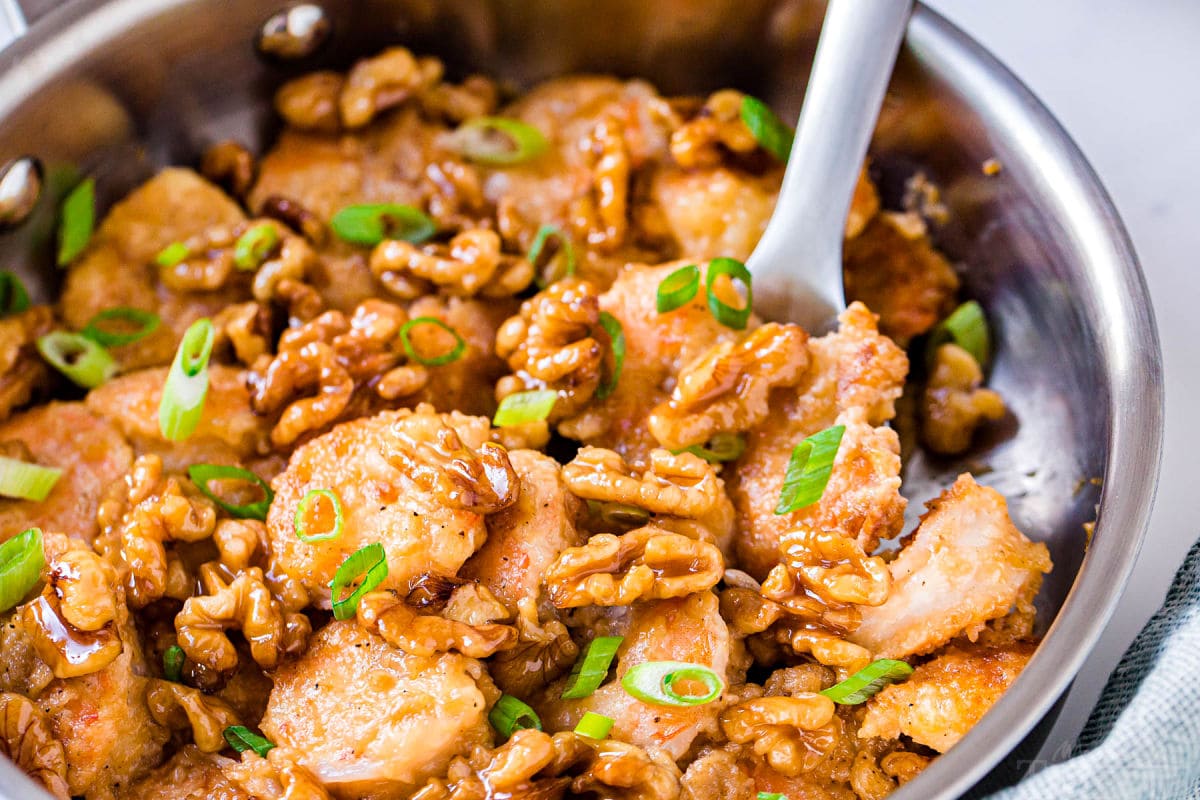 shot of honey walnut shrimp still in the skillet with a scoop being removed