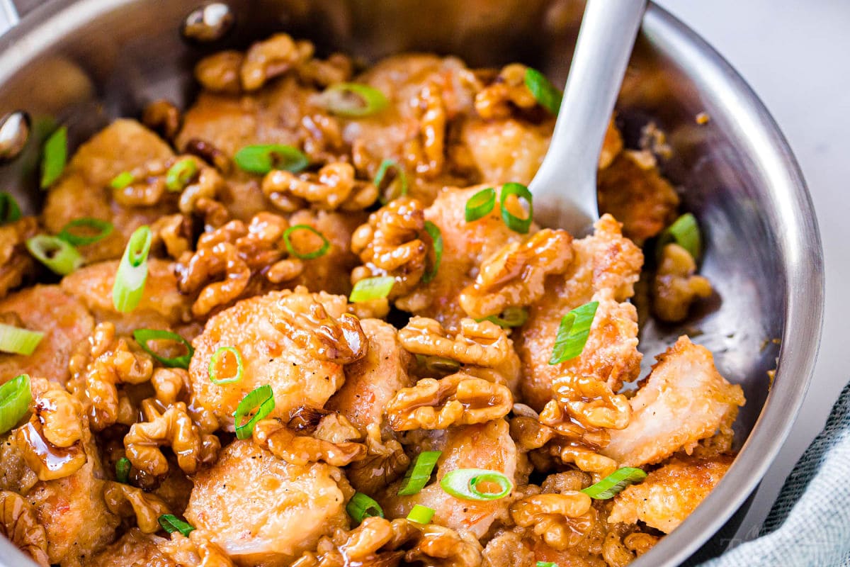 shot of honey walnut shrimp still in the skillet with a scoop being removed 