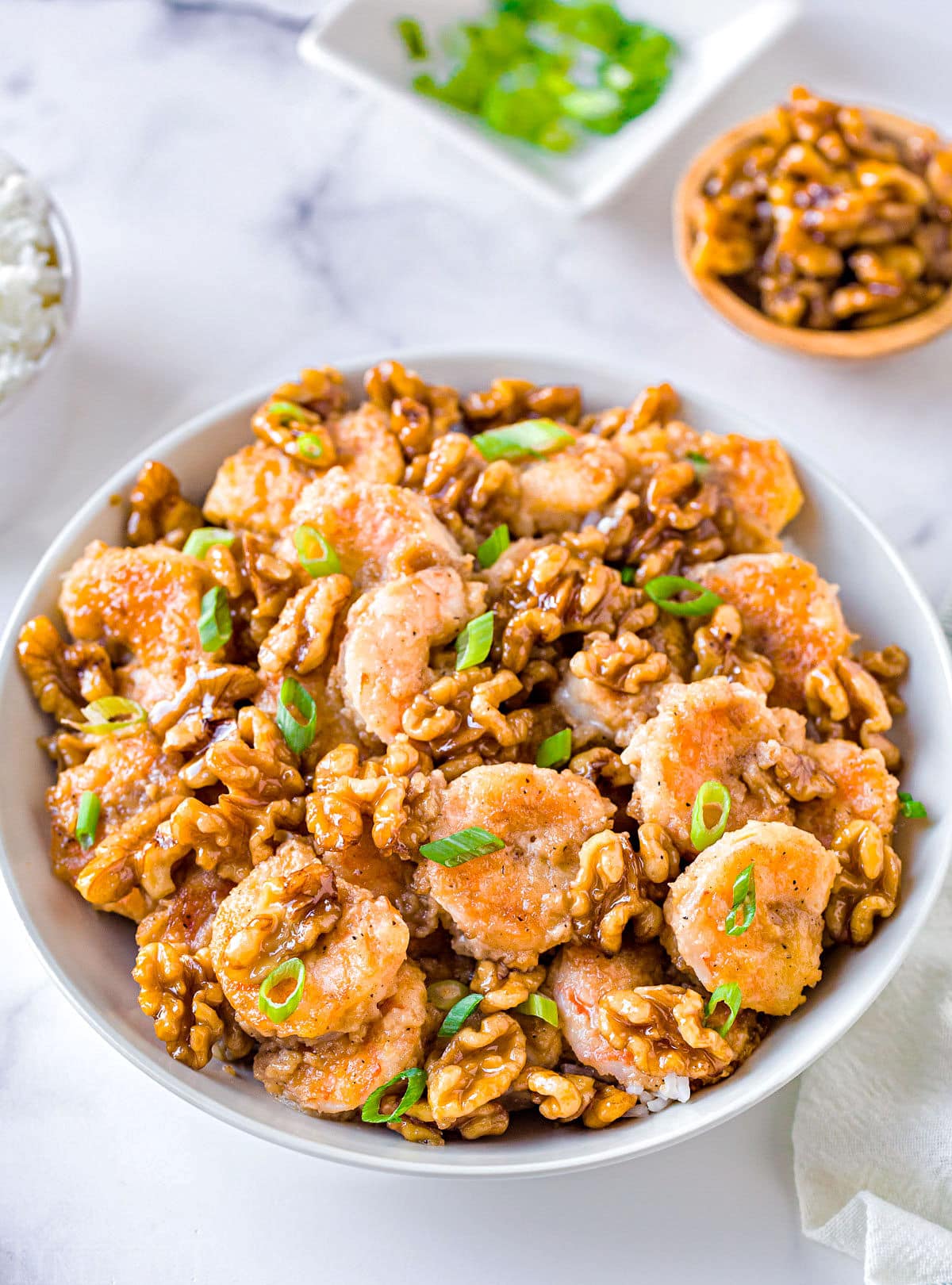 white bowl filled with honey walnut shrimp with small bowl of walnuts and green onions in background