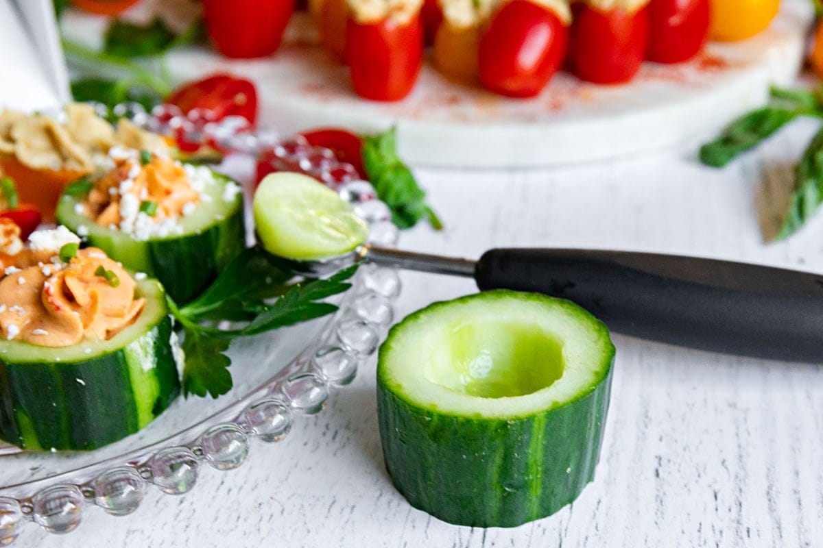 cucumber cup with melon baller next to a plate of hummus stuffed veggies