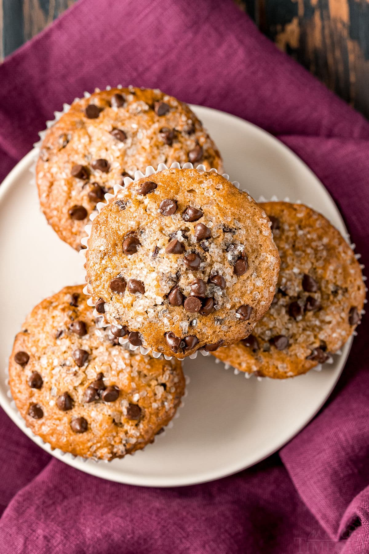 top down view chocolate chip muffins on white plate sitting on burgundy napkin