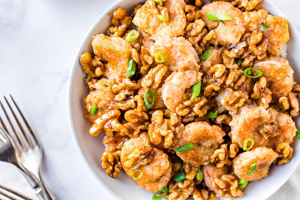 top down view of honey walnut shrimp in white bowl with forks near it on the left side and the dish is garnished with green onion