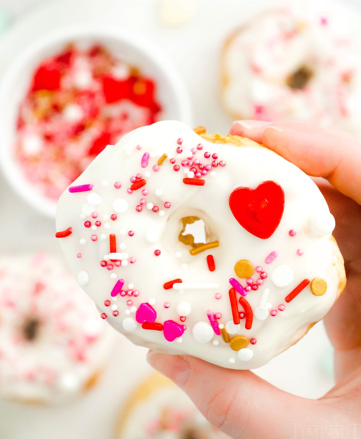 decorated donut being held up over a tray of donuts