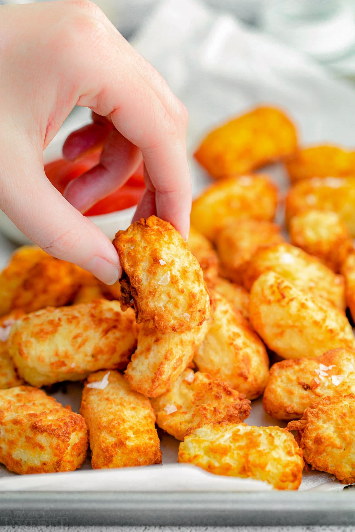 tater tot being picked up off a sheet pan full of tots.