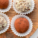 four truffles sitting on wood board each in individual white paper cups.