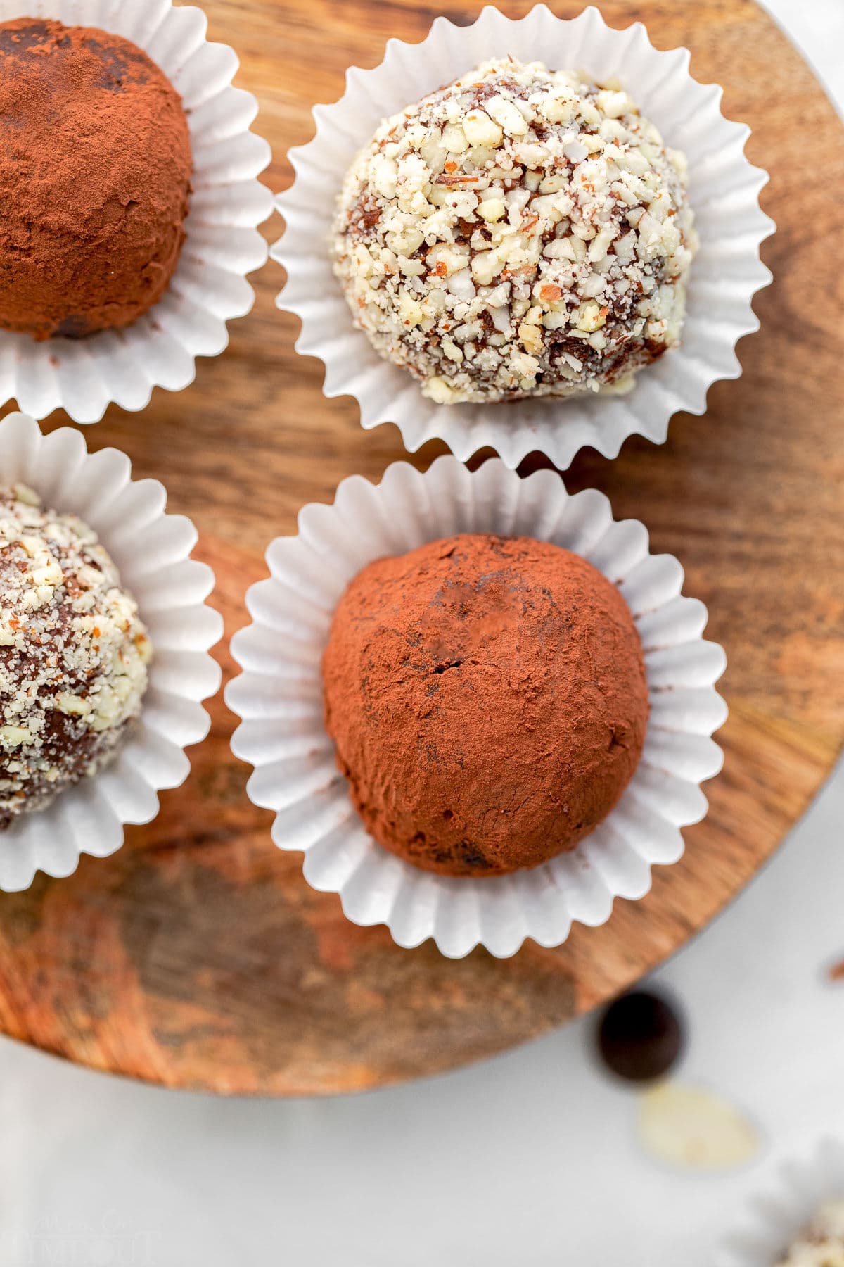 four truffles sitting on wood board each in individual white paper cups.