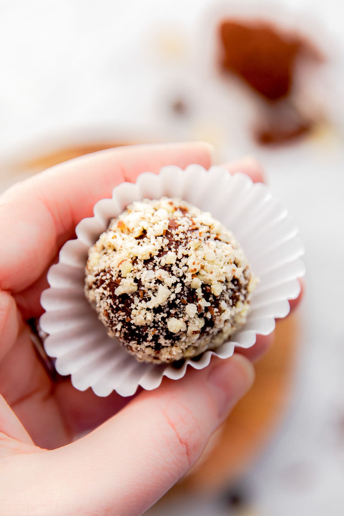 hand holding truffle rolled in almonds in white liner.