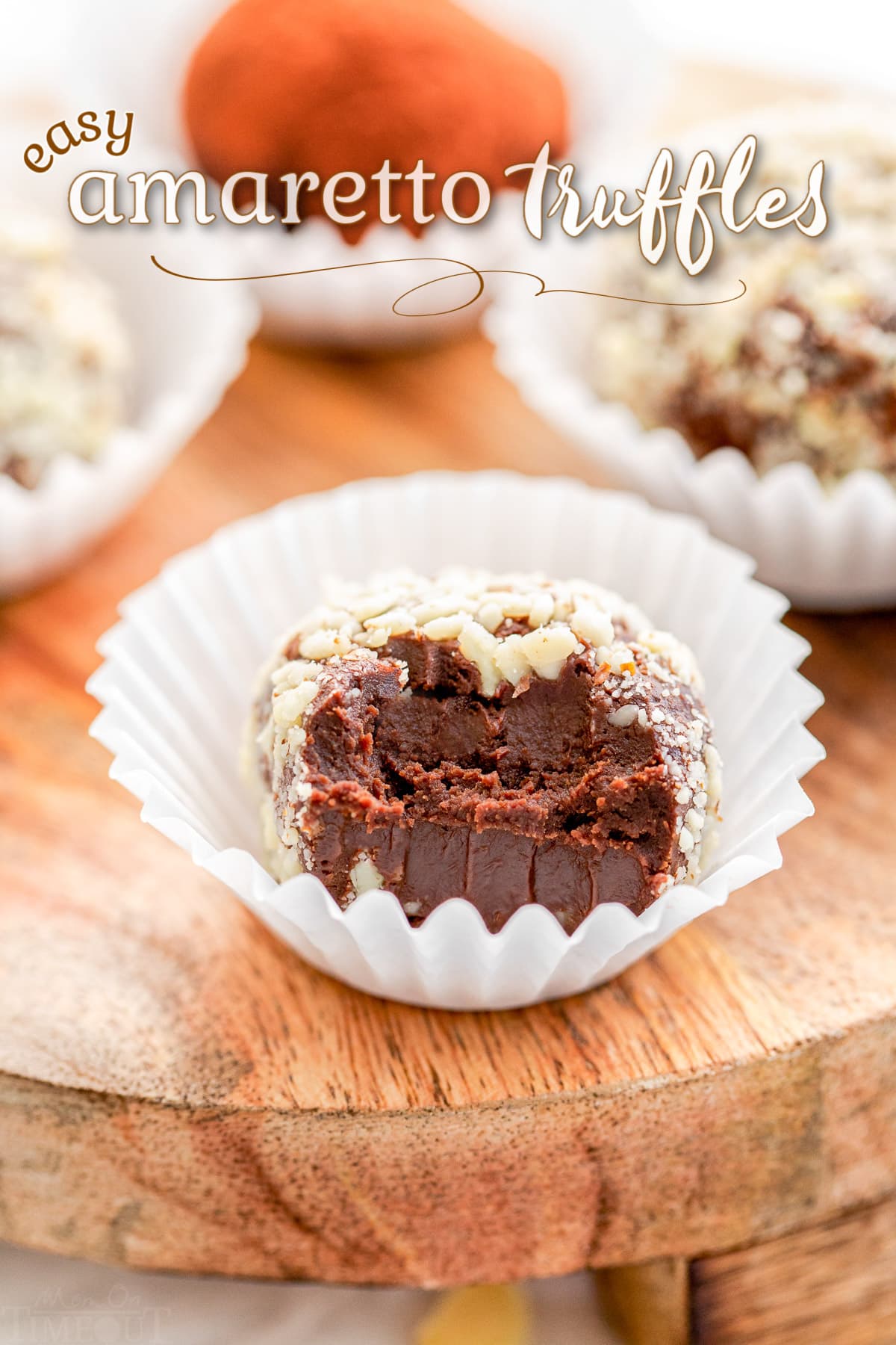 amaretto truffle with bite taken in white paper liner sitting on wood board with title overlay at top of the image.