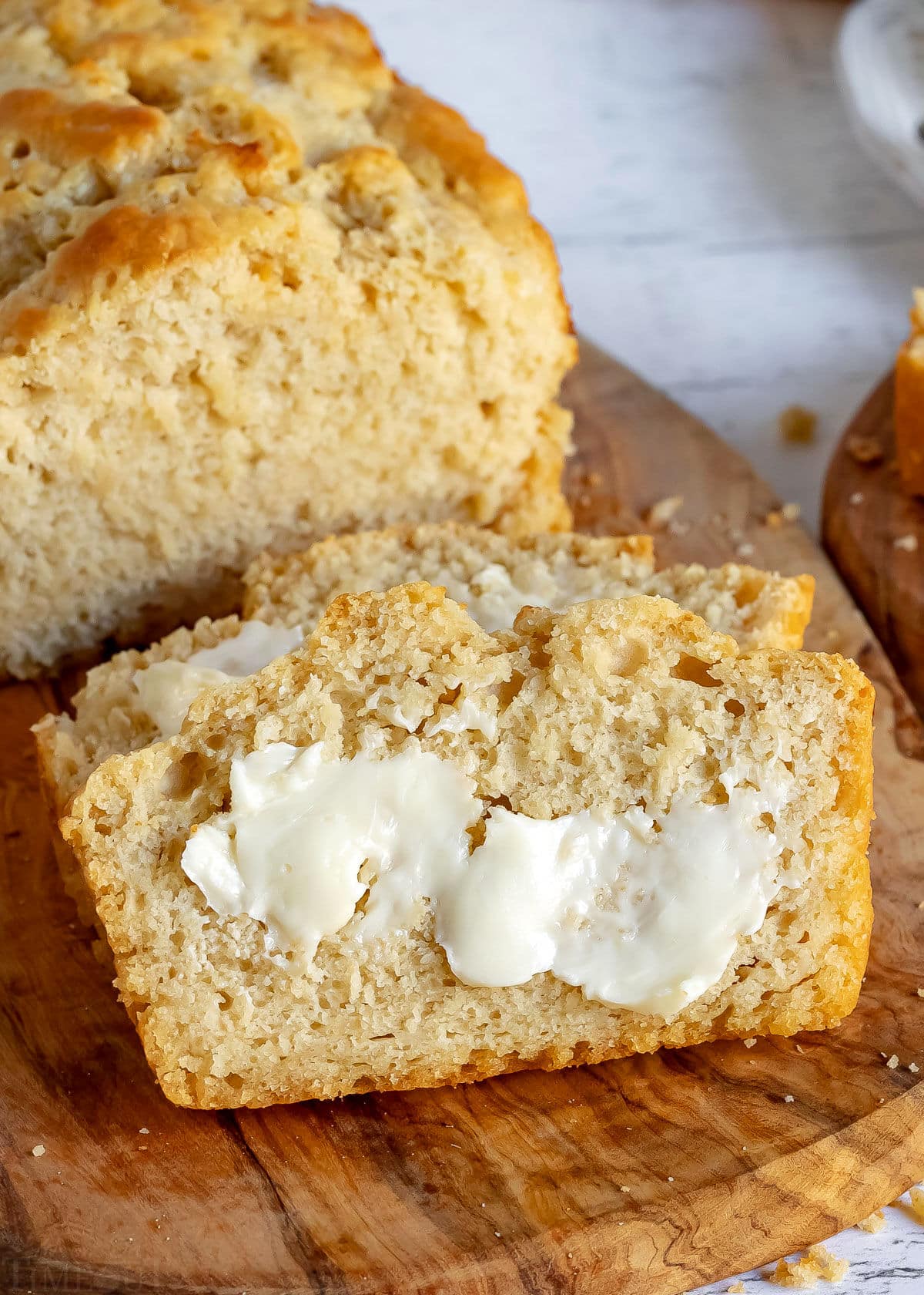 slice of beer bread with butter on it leaning up against loaf bread.