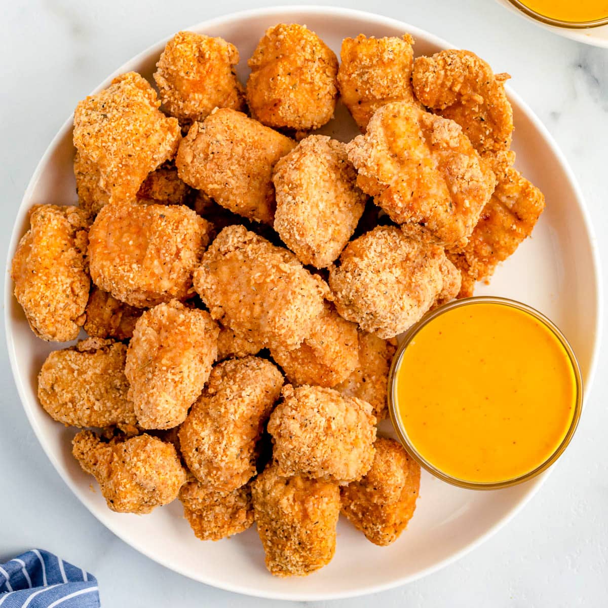 chicken nuggets piled high on a plate with dipping sauce.