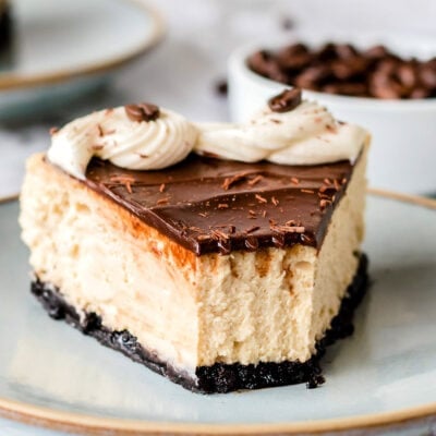 piece of cheesecake on pottery plate topped with ganache and frosting