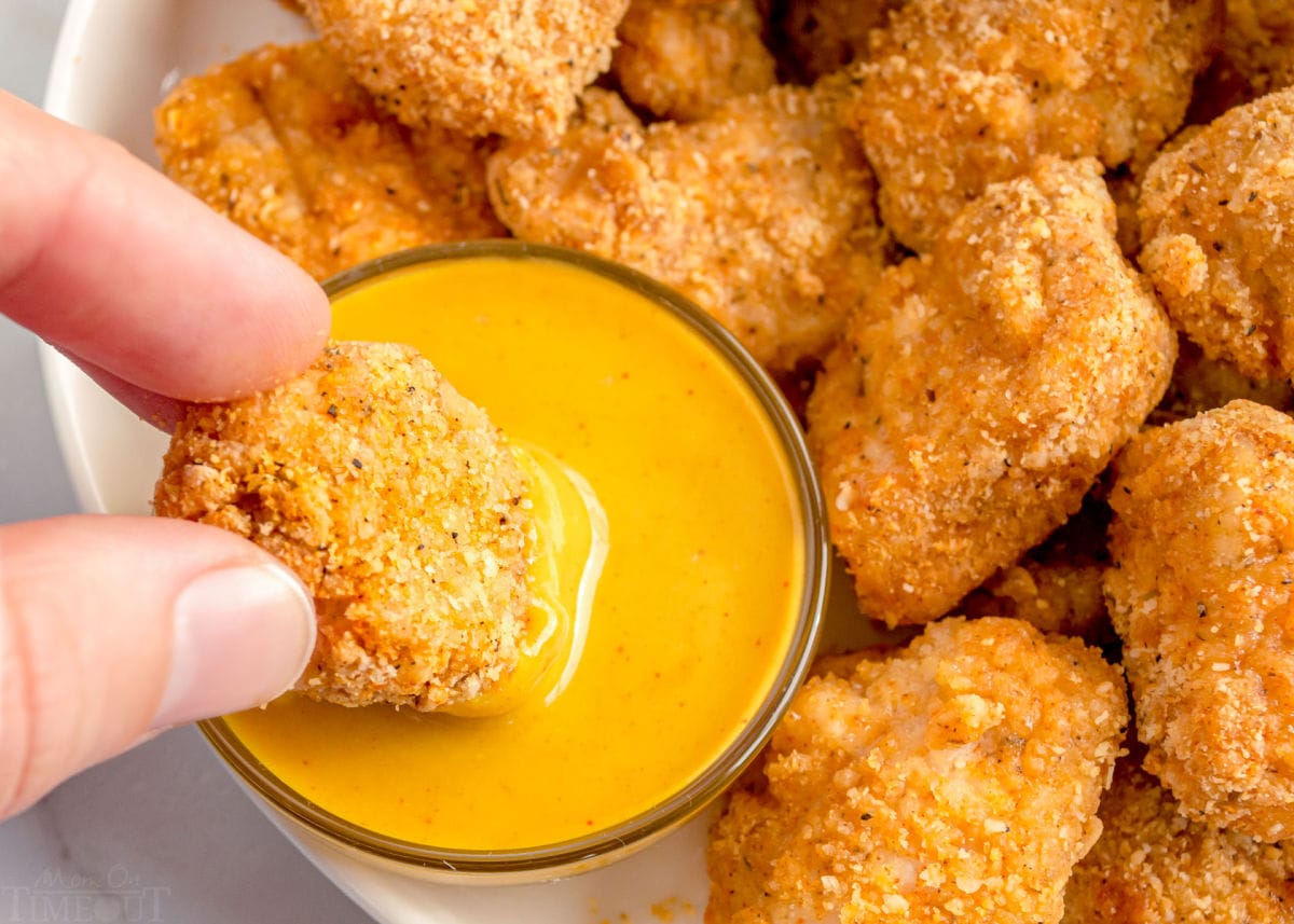 chicken nuggets being dipped in honey mustard sauce.