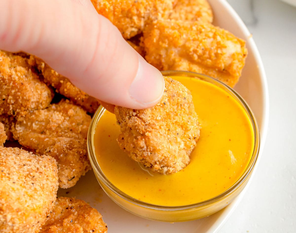 chicken nuggets being dipped in honey mustard sauce.