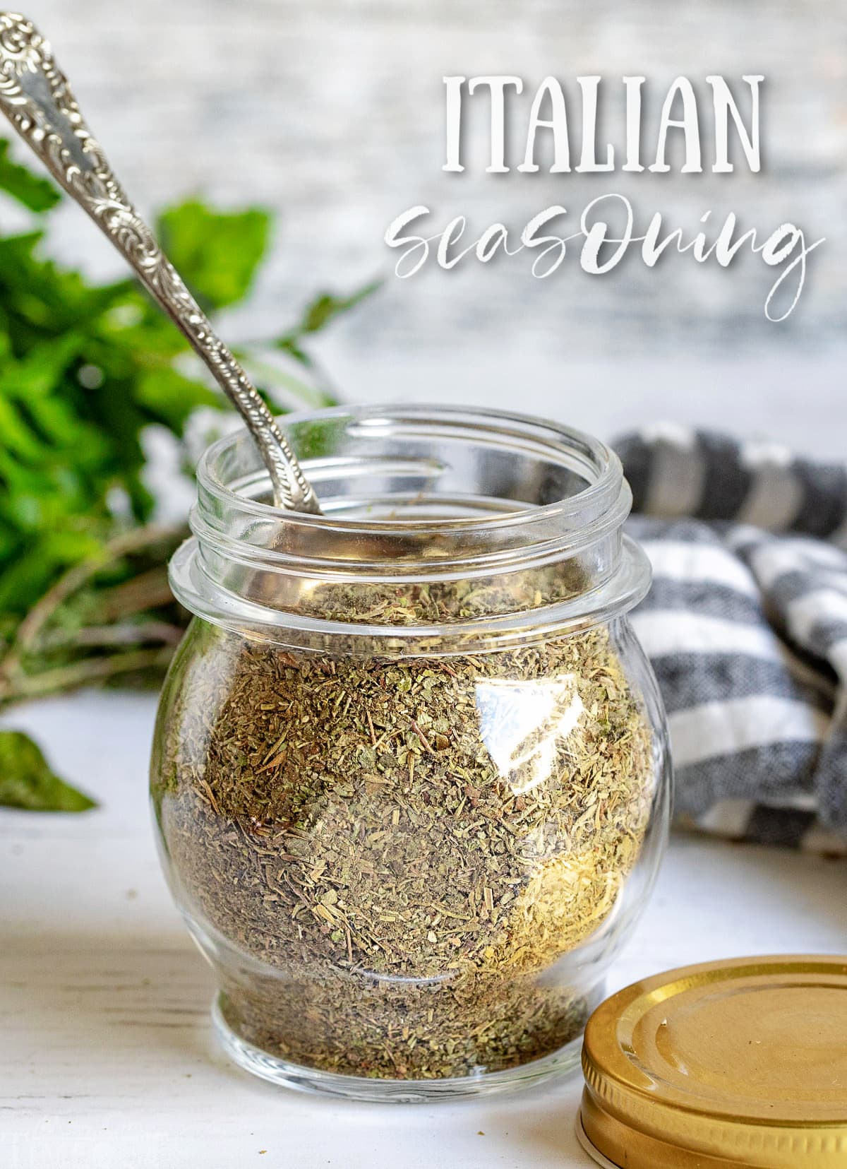 italian seasoning in a small glass jar with a spoon in the jar and title at top of image.