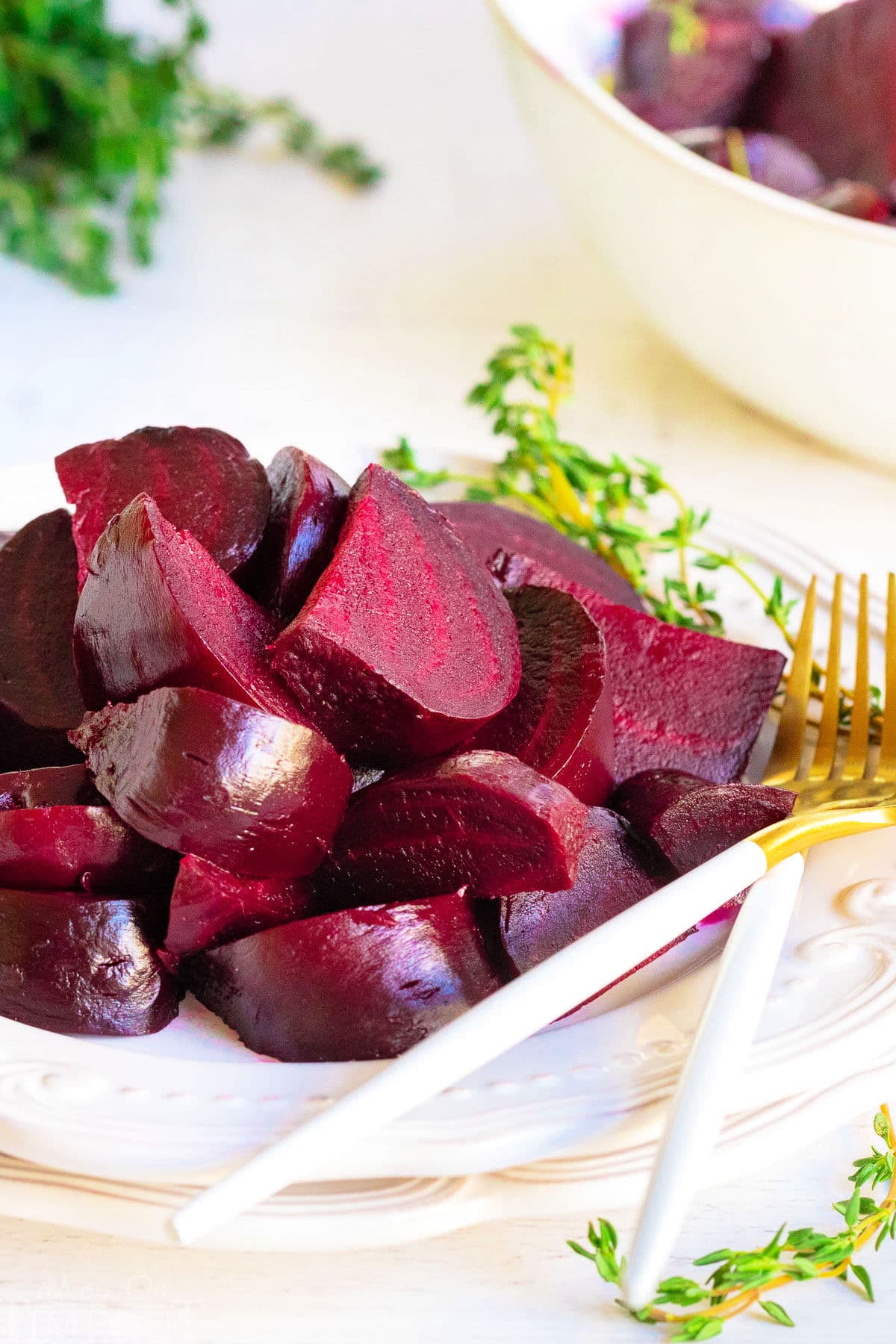 roasted beets cut up and arranged on white plate with thyme in background.