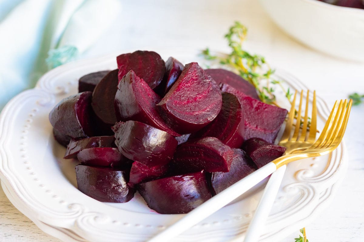 white plate with roasted beets and a couple of gold forks.