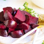 roasted beets cut up and arranged on white plate with white and gold forks and thyme in background.