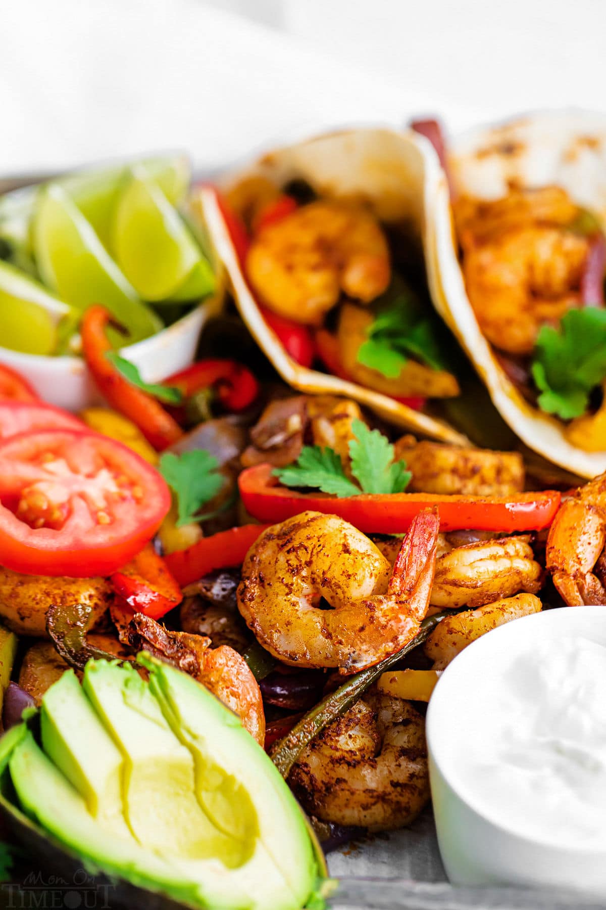 close up look at the shrimp fajitas on sheet pan with sliced avocado and sour cream.