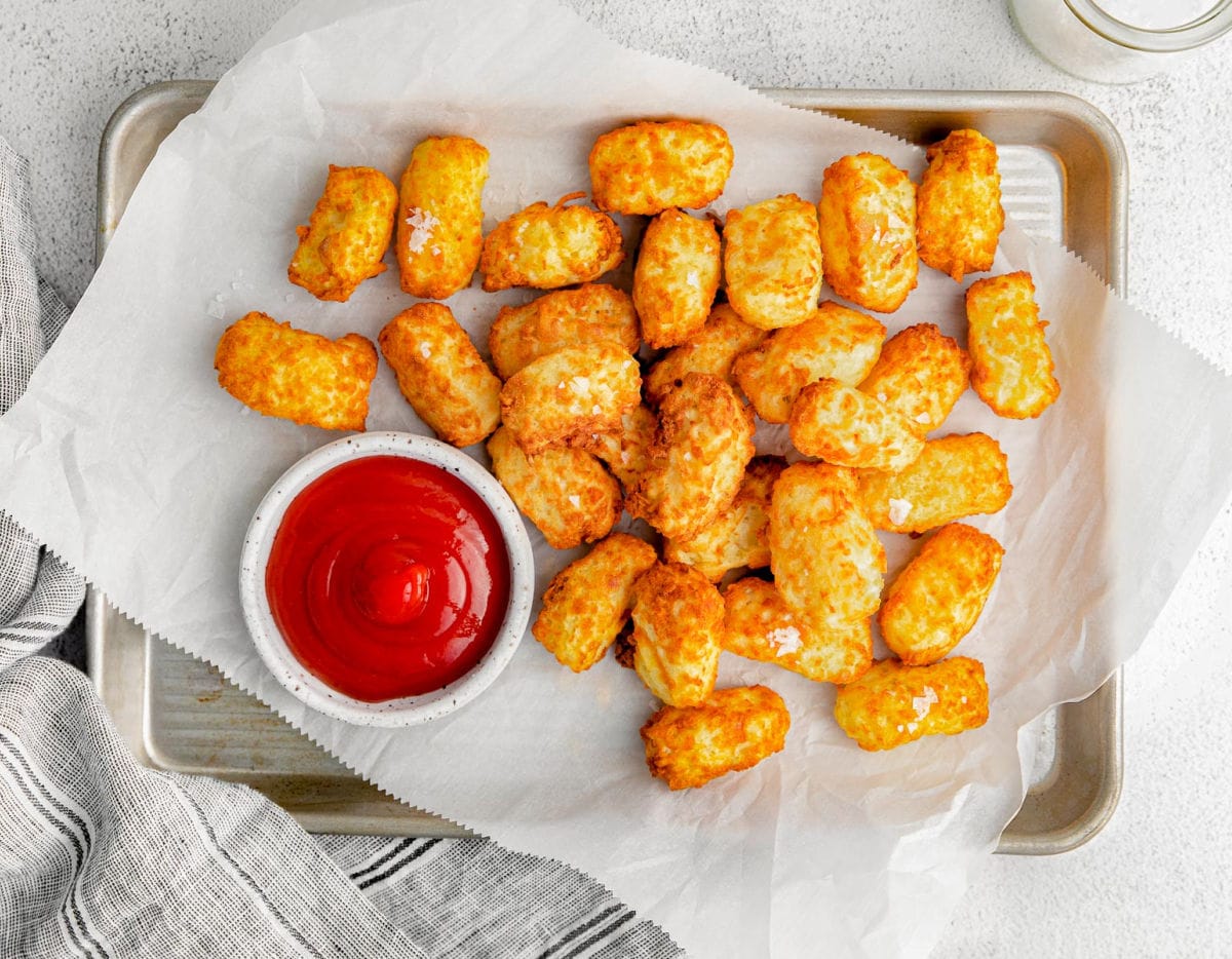 top down look at tater tots on white parchment paper with a bowl of ketchup to the side.