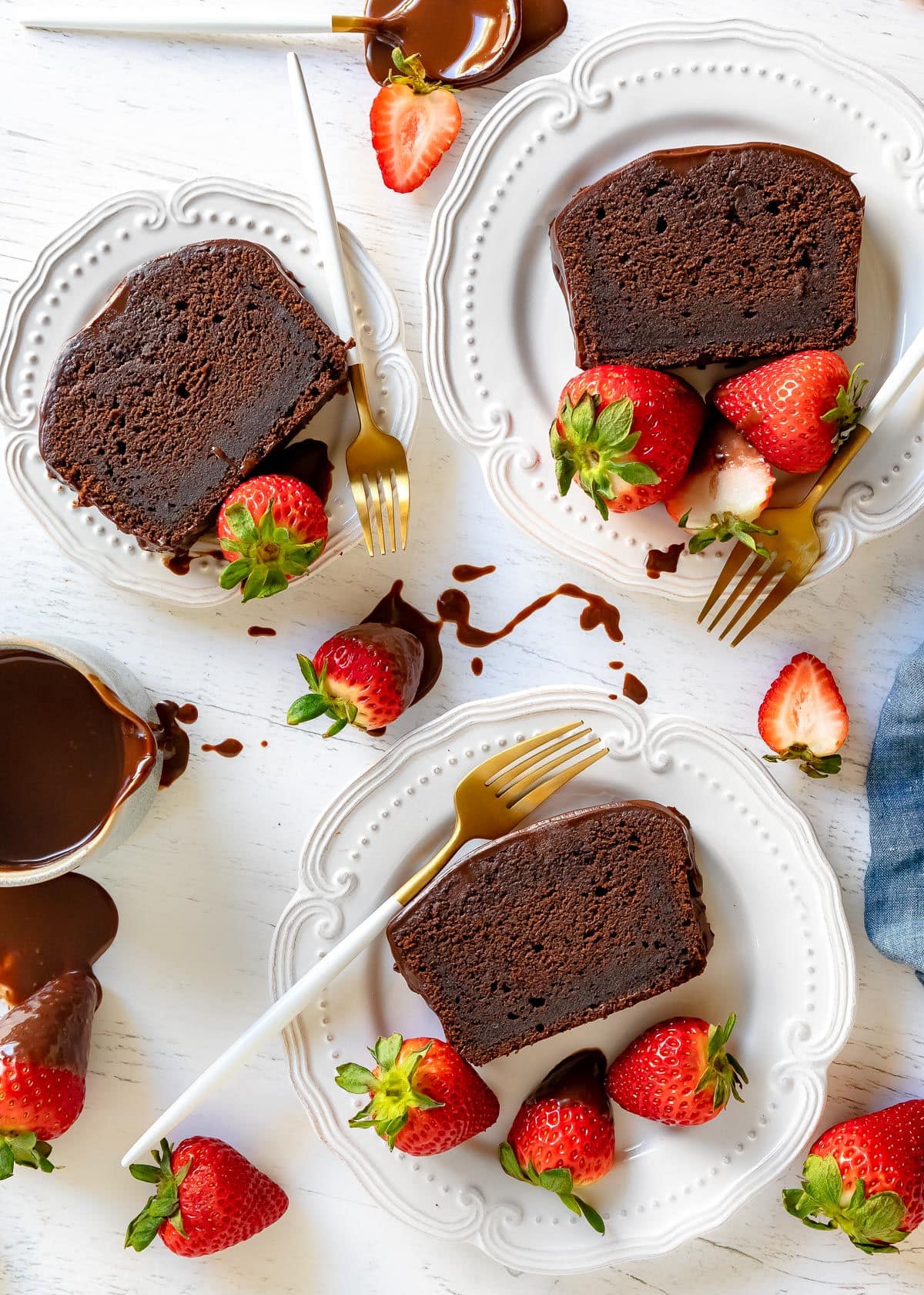 top down view of three slices of pound cake on white plates with strawberries scattered about and white and gold forks on plates